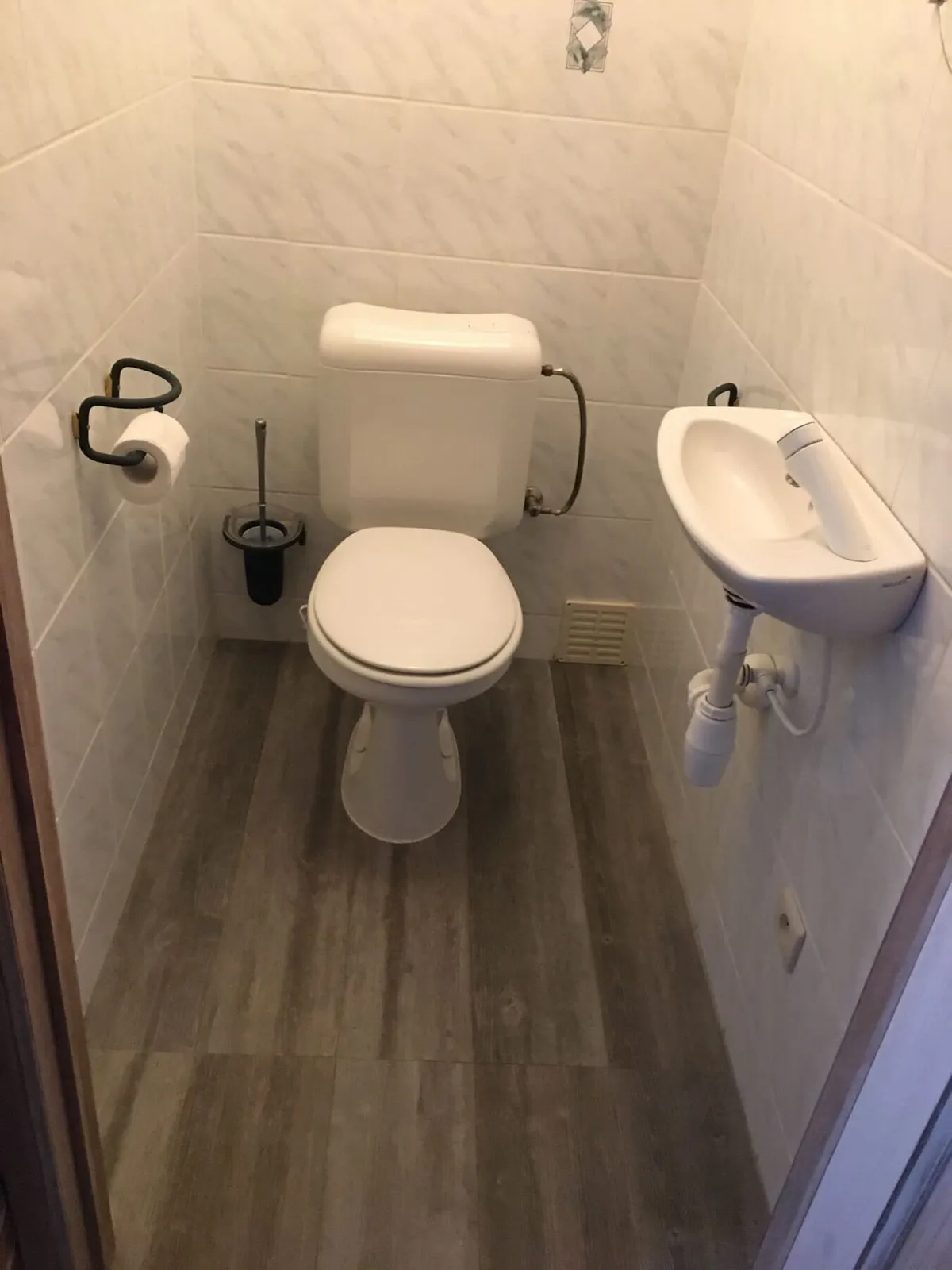 Anciennes toilettes avec carrelage blanc et lave-mains avant la rénovation à Anvers