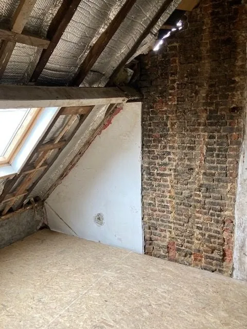 Grenier brut avec mur en briques et charpente avant la rénovation à Anvers