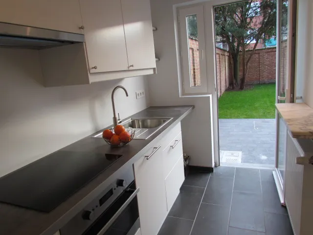 Cuisine blanche rénovée avec porte vers le jardin – IDGS Constructions, région de Bruxelles